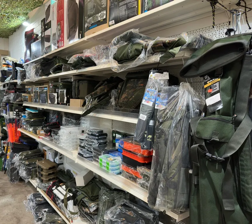 Lagerregal mit verschiedenen Outdoor- und Angelzubehörartikeln wie Taschen, Rutenhaltern und Aufbewahrungsboxen in Plastikverpackungen.