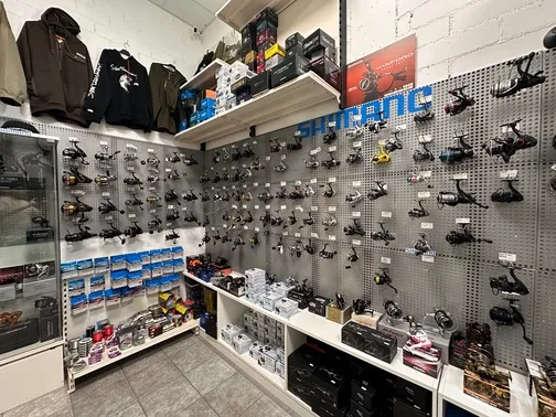 Laden mit Angelrollen, Angelzubehör und Jacken an den Wänden in einem fachmännisch organisierten Angelgeschäft.