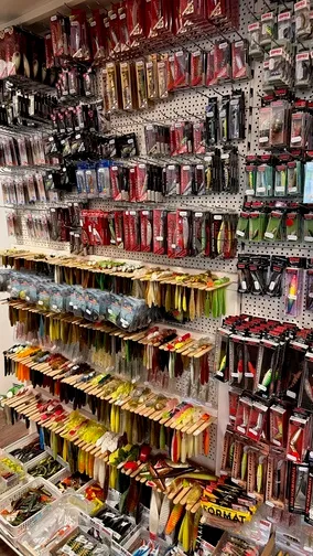 Wand mit verschiedenen Arten von Angelködern in Verpackungen und Boxen in einem Angelgeschäft.