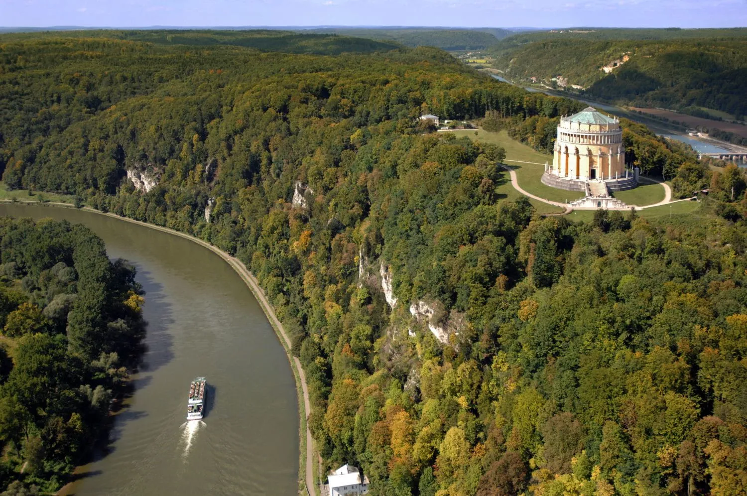 Luftaufnahme des Donauflusses mit grün bewaldeten Hügeln und dem historischen Befreiungshalle-Gebäude auf einem Hügel in Deutschland.