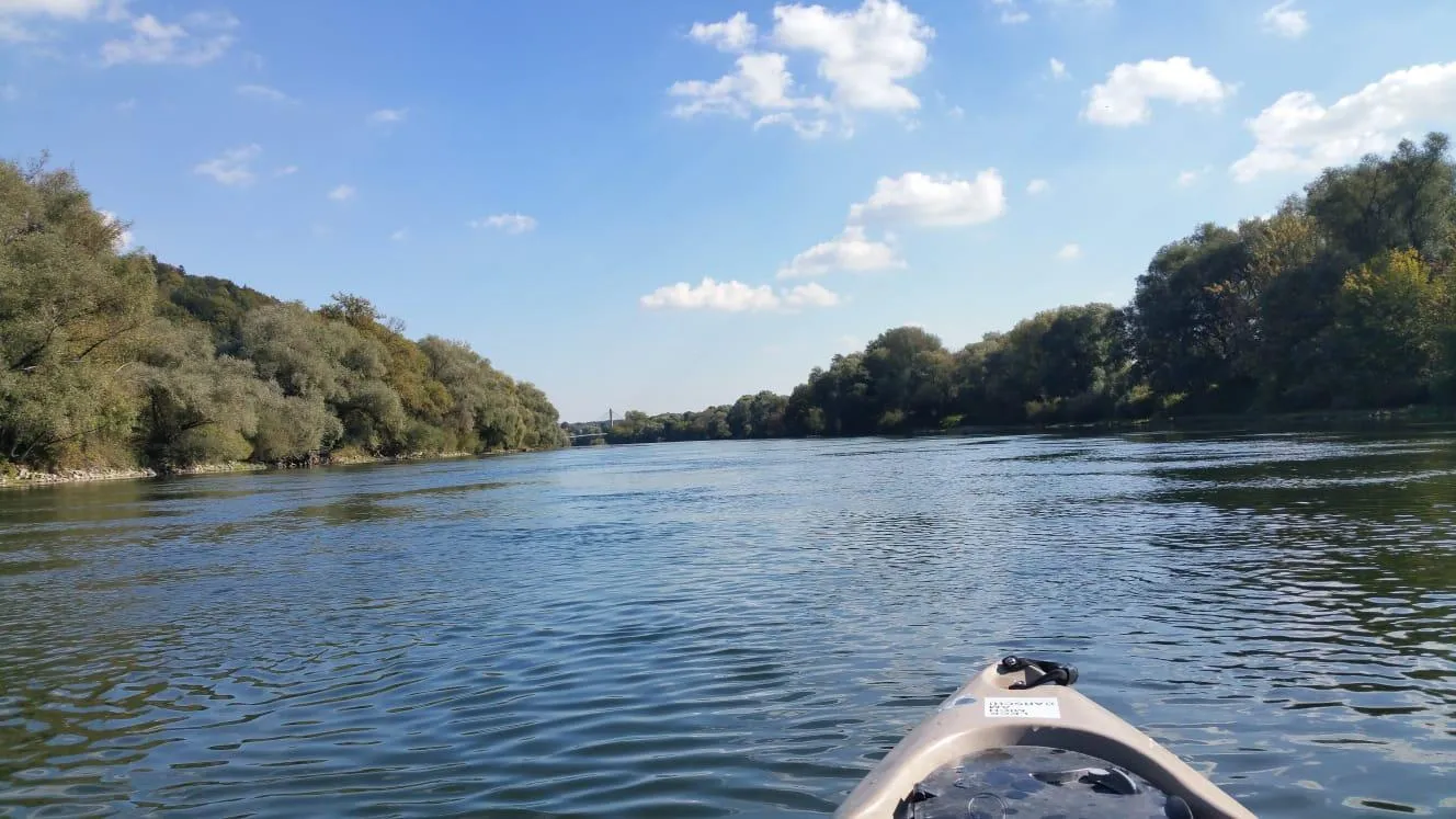 Blick von einem Kanu auf einen ruhigen Fluss mit Bäumen an beiden Ufern unter einem blauen Himmel mit wenigen Wolken.