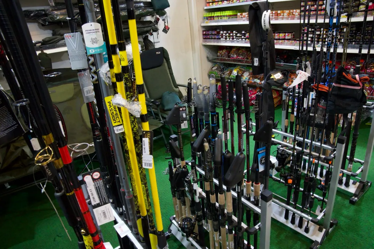 Verschiedene Angelruten und Angelzubehör in einem Geschäft auf grüner Teppichfläche.