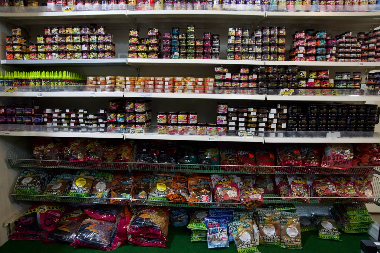 Regale in einem Geschäft, gefüllt mit verschiedenen Angelködern und Fischfuttermitteln in Dosen, Flaschen und Verpackungen.