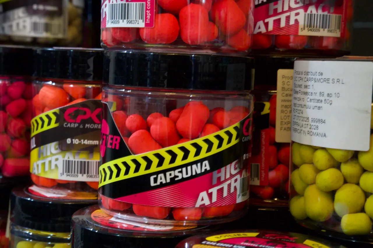 Mehrere transparente Plastikbehälter mit roten und gelben Karpfenködern, teilweise mit Etiketten, die "HIGH ATTRACT" und "CAPSUNA" zeigen.
