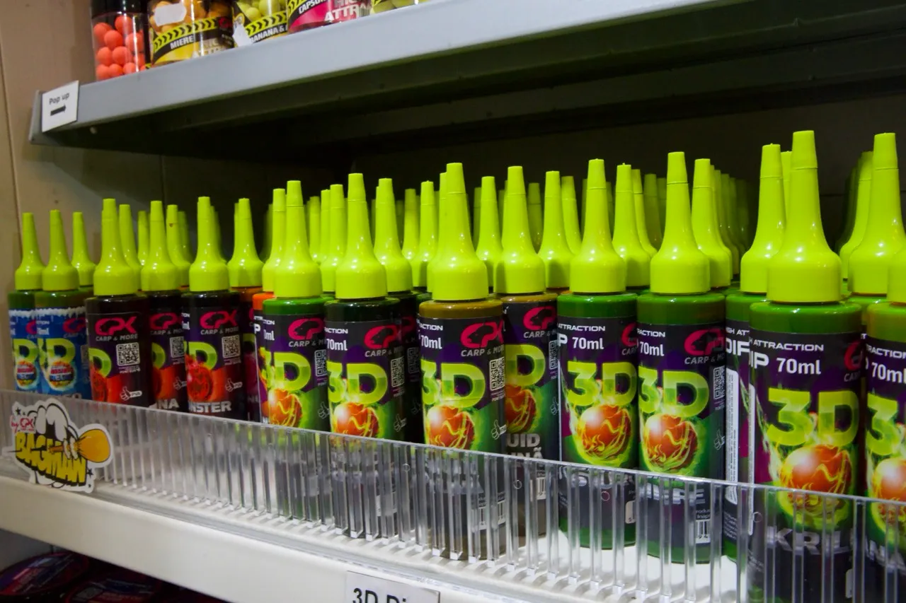 Regal mit mehreren Reihen von 70 ml 3D Carp & More Angelsaucen-Flaschen mit gelb-grünen Tropfspitzen.