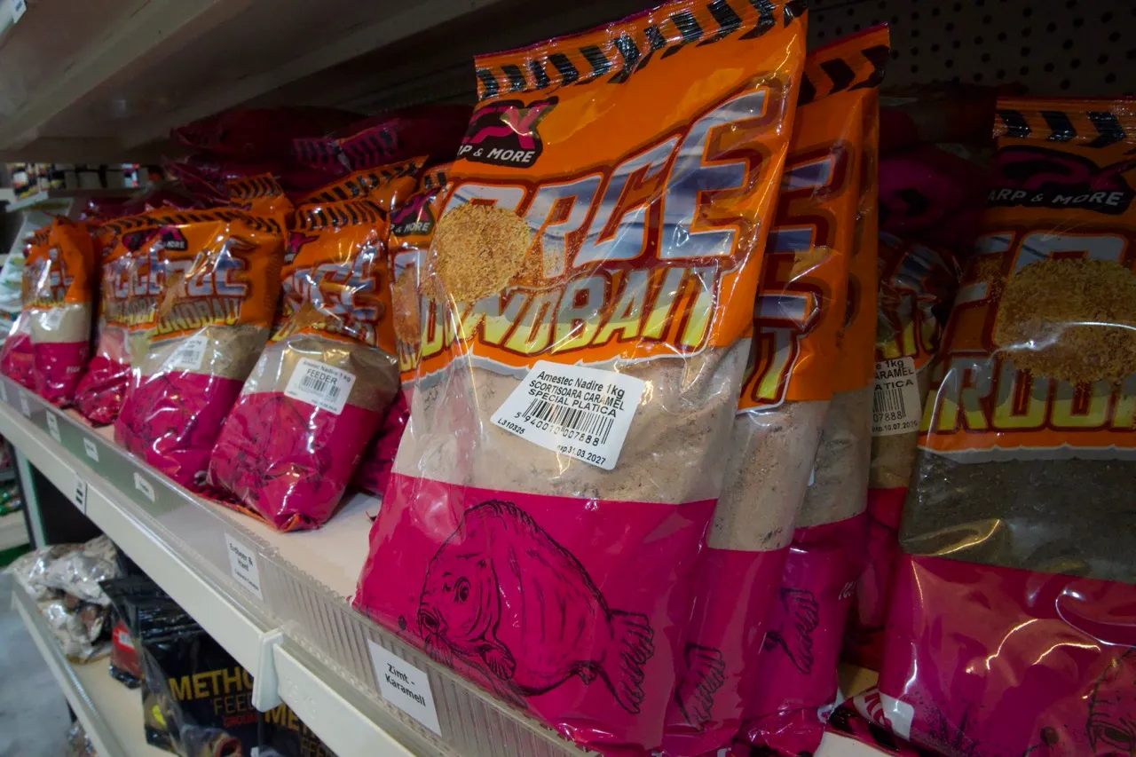 Mehrere orange-rosa verpackte Tüten mit Fischköder stehen in einem Ladenregal.