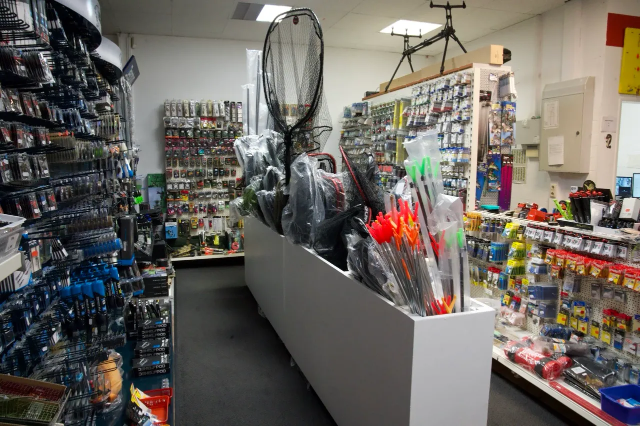 Innenansicht eines Angelgeschäfts mit Angelnetzen, Leuchtpfeilen und vielfältigem Angelausrüstungszubehör an Regalen und Wänden.