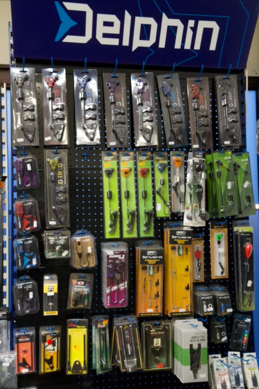 Angelzubehör wie Bissanzeigen und Rutenhalter auf einem schwarzen Wanddisplay mit Delphin-Logo.