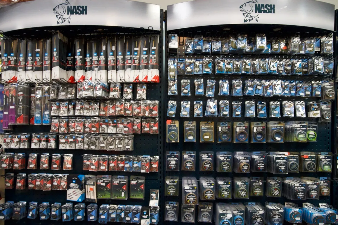 Zwei Regale mit angelausrüstung von Nash, darunter Angelruten und verschiedene Angelzubehörteile in Verpackungen.