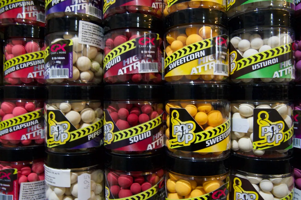 Verschiedene Gläser mit bunten Pop-Up Ködern für das Karpfenangeln, beschriftet mit Aromen wie Squid, Sweetcorn und Usturoi.