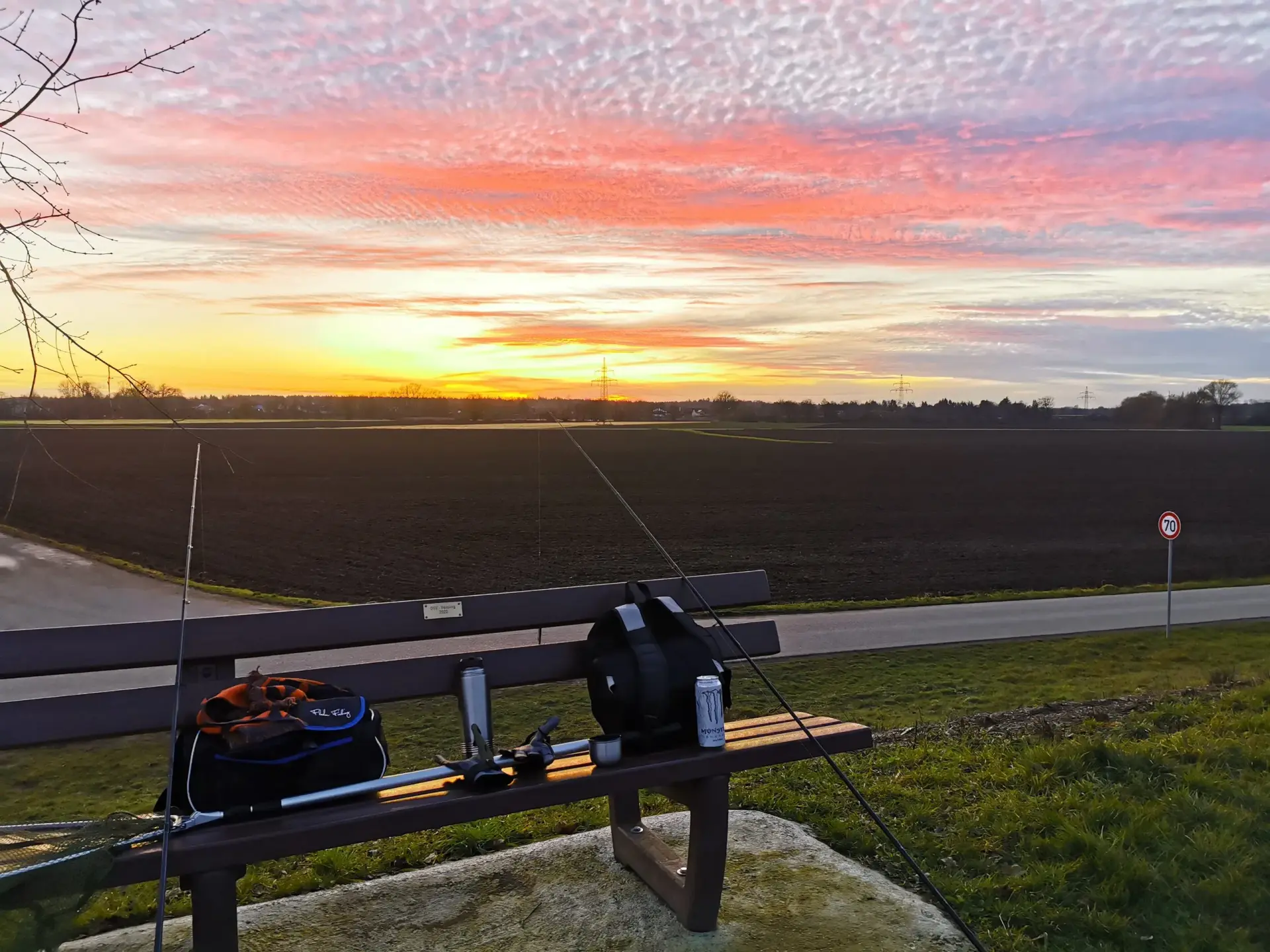 Bank mit Angelausrüstung bei Sonnenuntergang über einem Feld