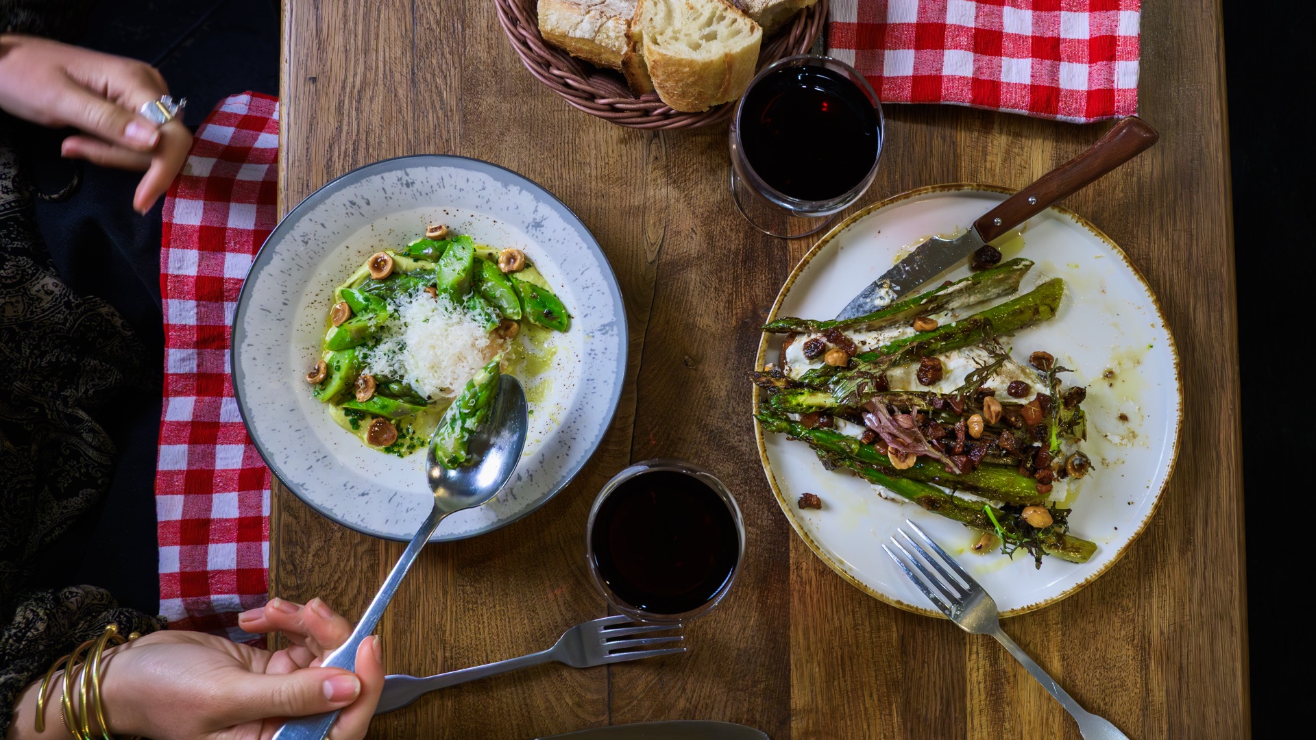 Two guests sharing green vegetable dishes and wine at a restaurant table