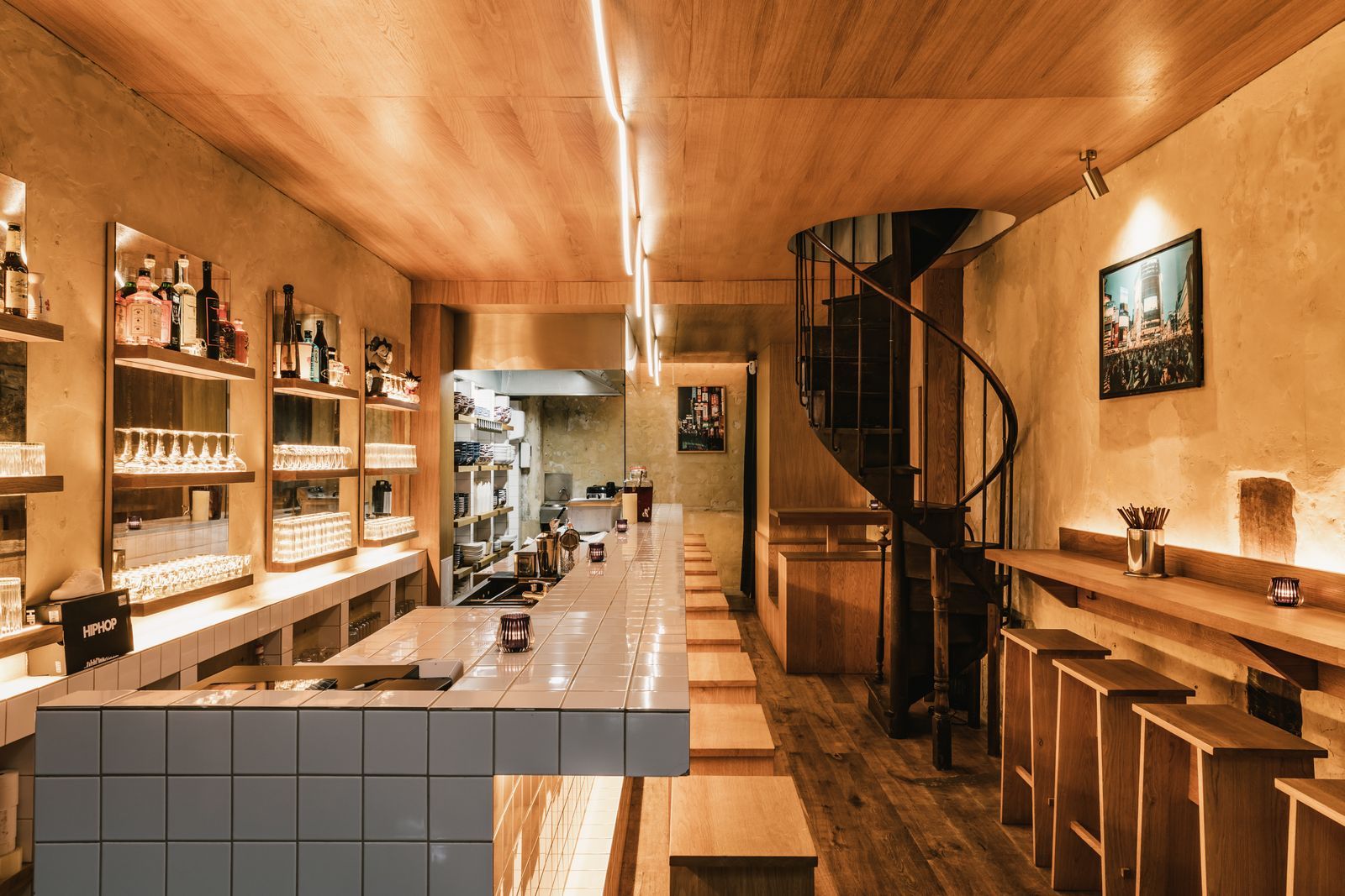 Warm restaurant interior with a tiled bar, open kitchen and spiral staircase