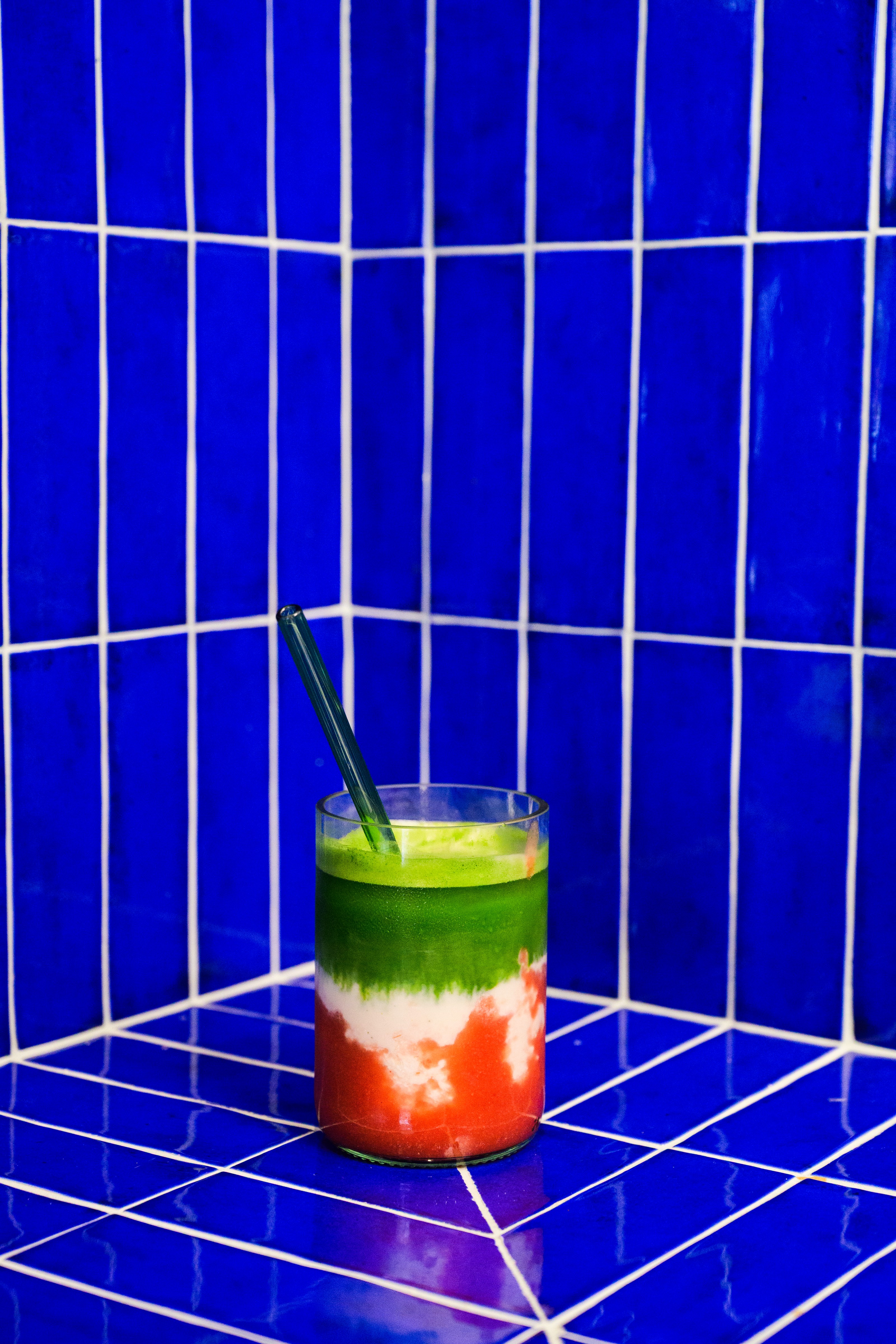 Layered green and red restaurant drink against a cobalt tile wall