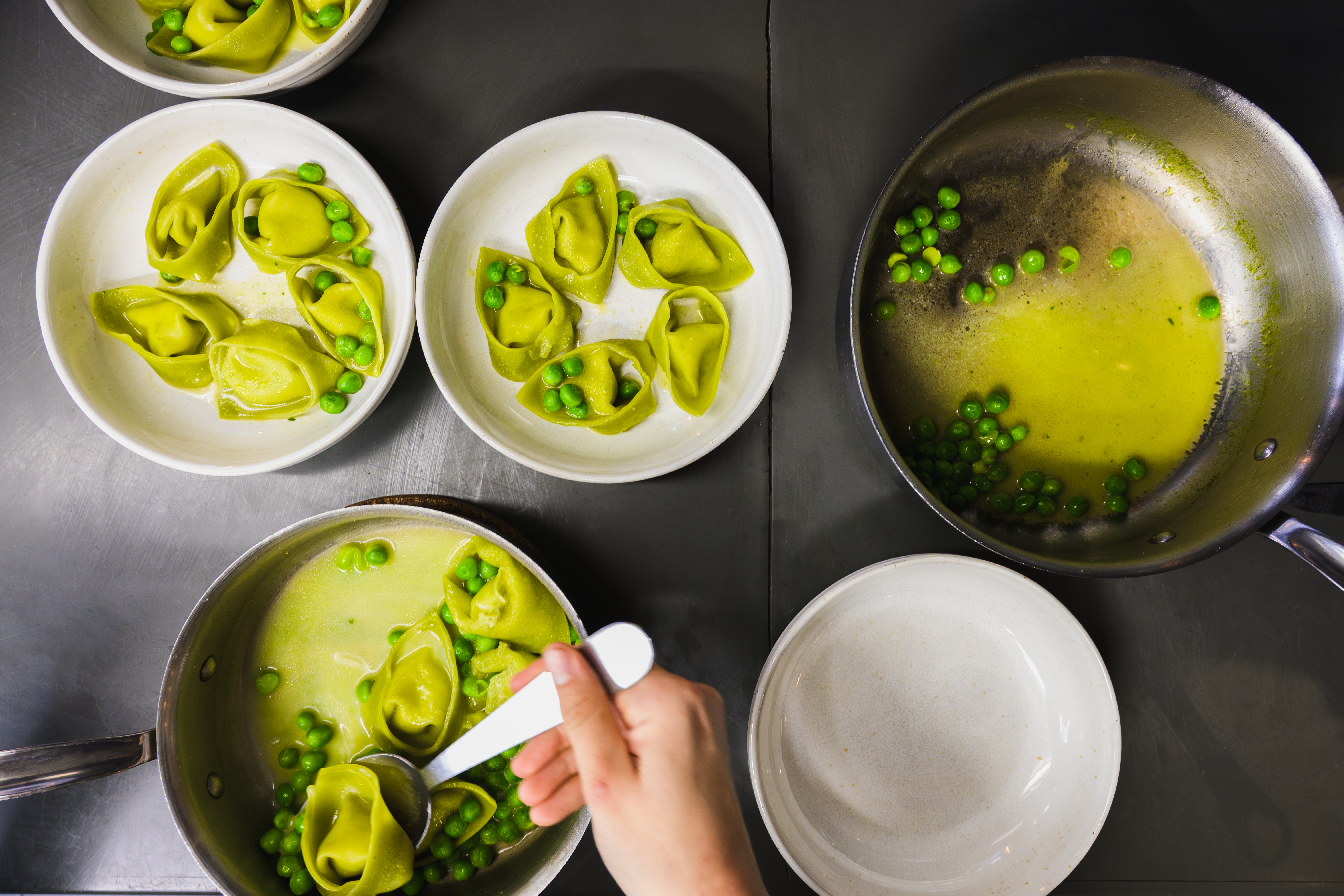 Green tortellini with peas being plated during restaurant service