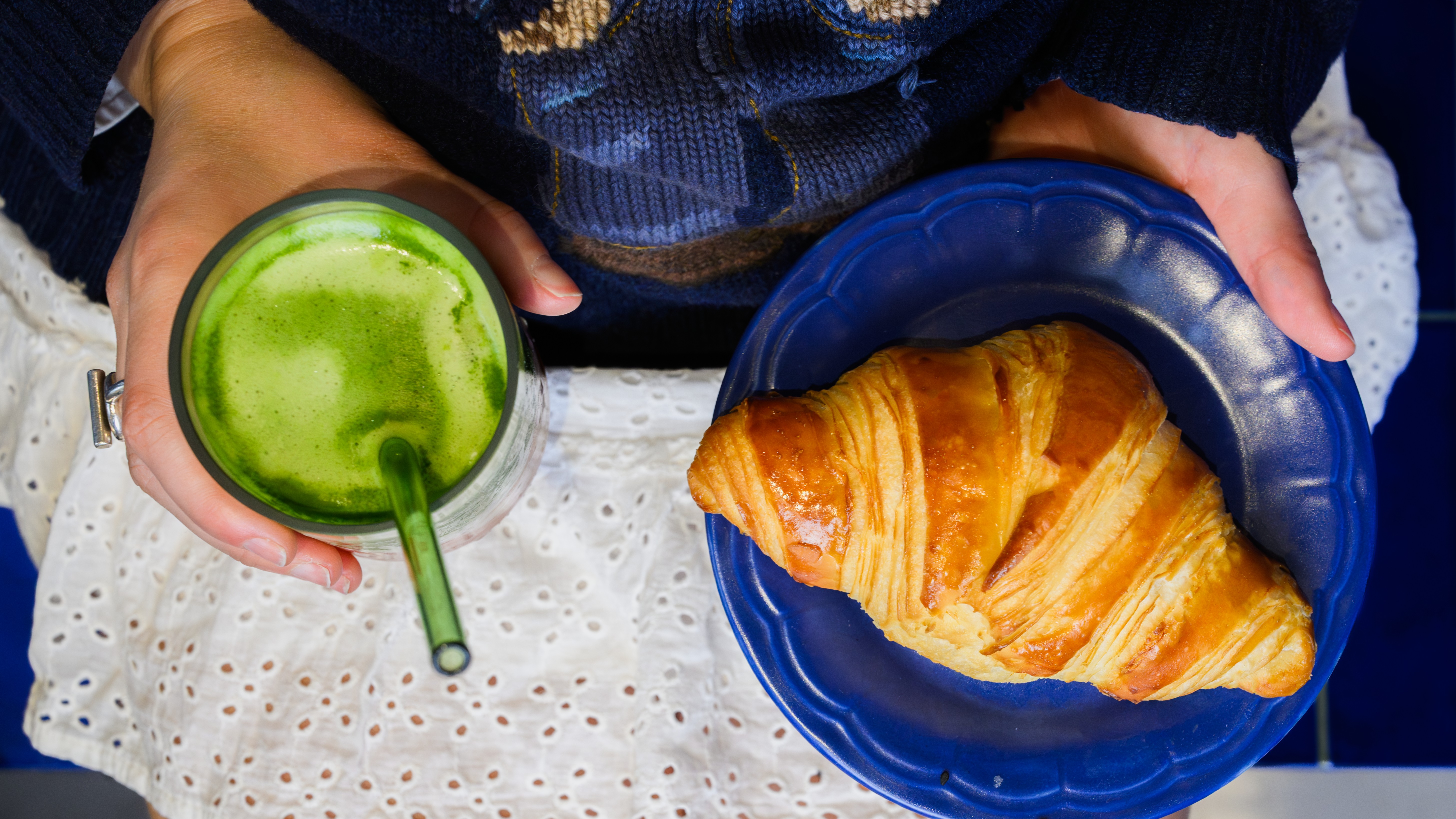 Guest holding a green drink and croissant on a blue restaurant table