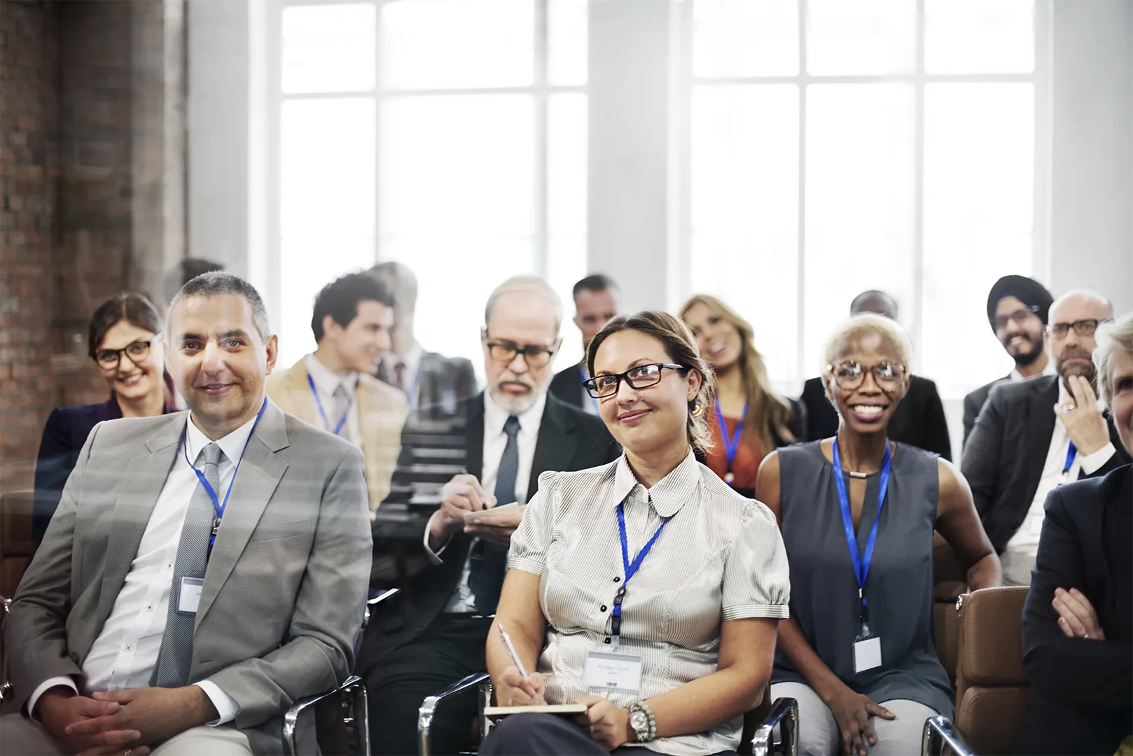 Diverse group of professionals wearing name badges attending a business seminar in a bright room.
