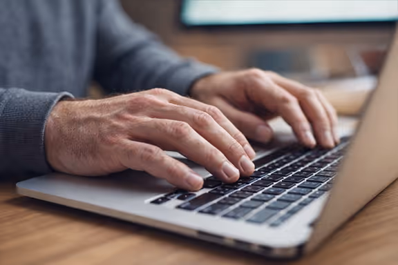 Close-up of hands typing on a laptop keyboard on a wooden desk.