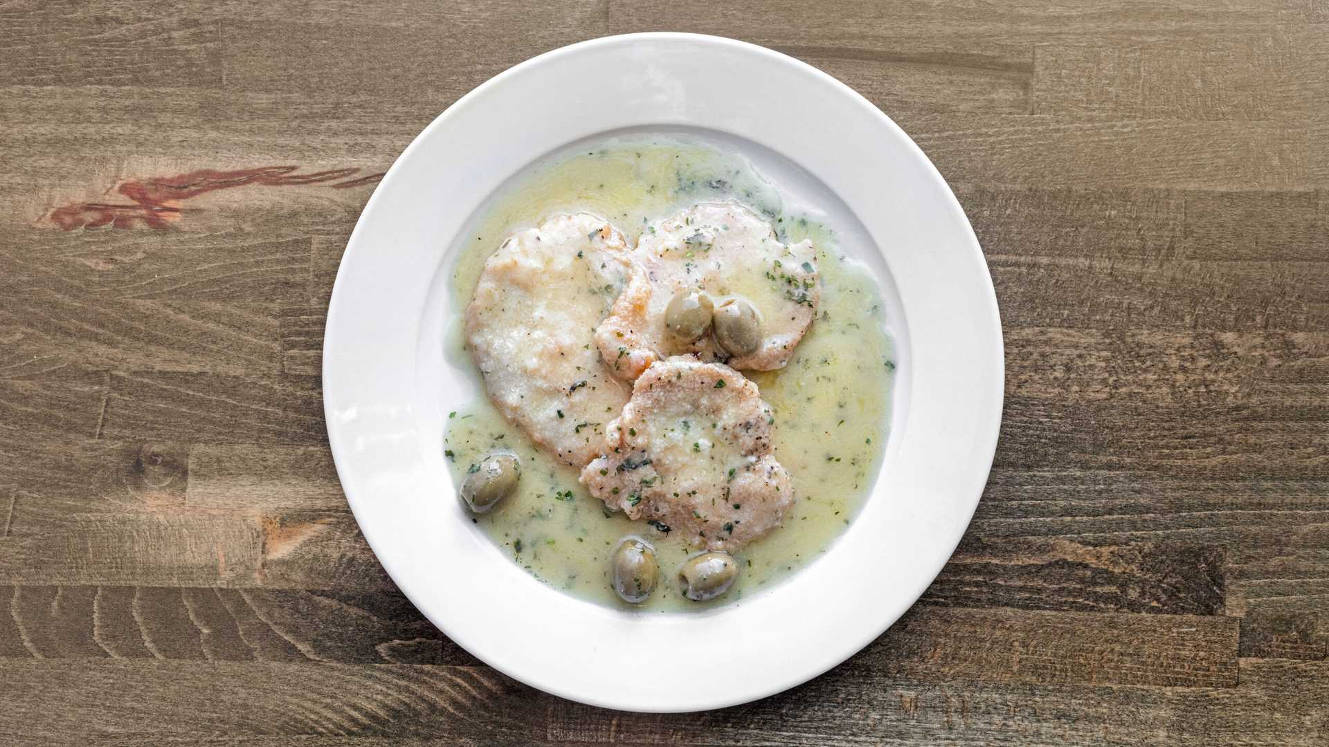 White plate with three pieces of chicken martini in a creamy green olive sauce on a wooden table.