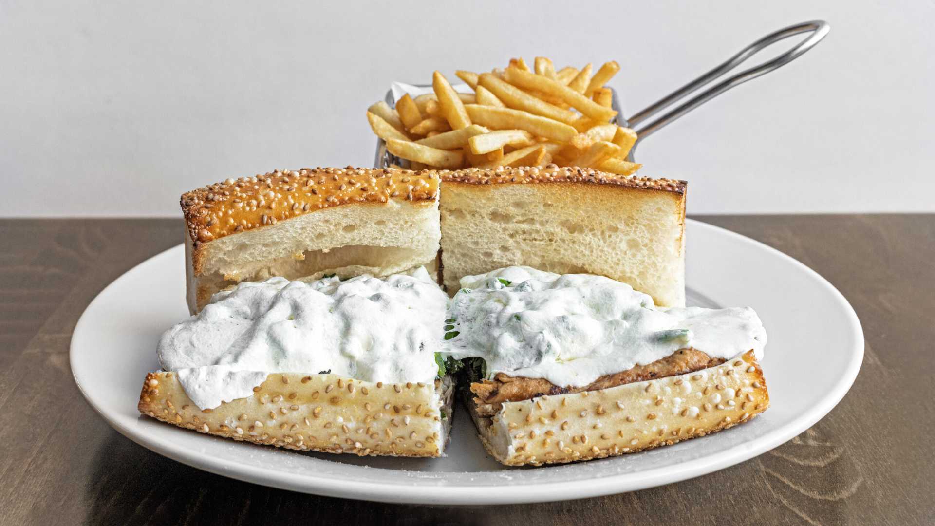 Sesame seed sandwich filled with grilled chicken and creamy white cheese, served with a side of French fries on a white plate.