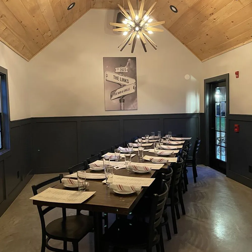 Indoor dining room with a long wooden table set with menus, plates, glasses, and napkins under a modern chandelier with wooden blades.