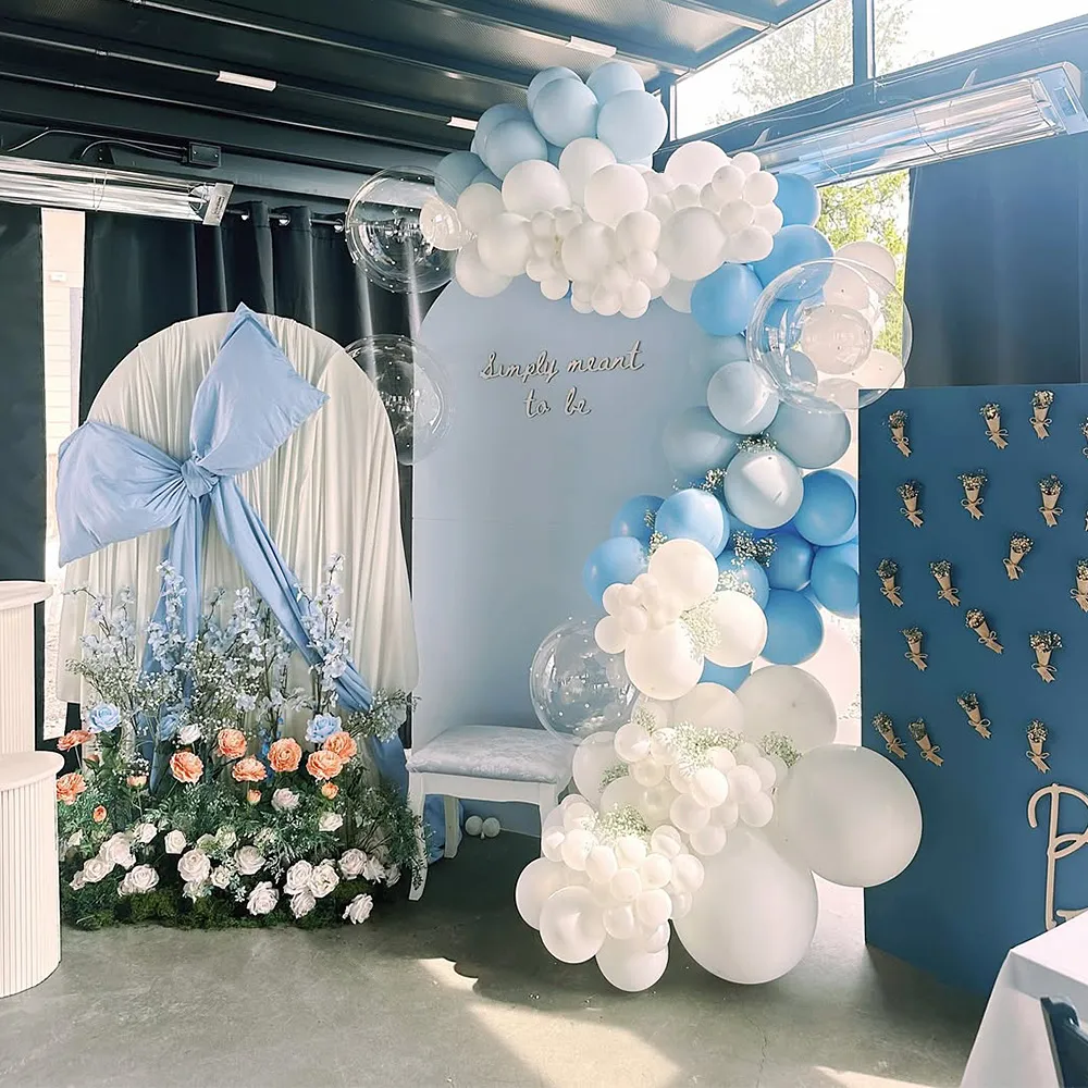 Event decoration with blue and white balloons arch, floral arrangements, and sign reading 'Simply meant to be'.