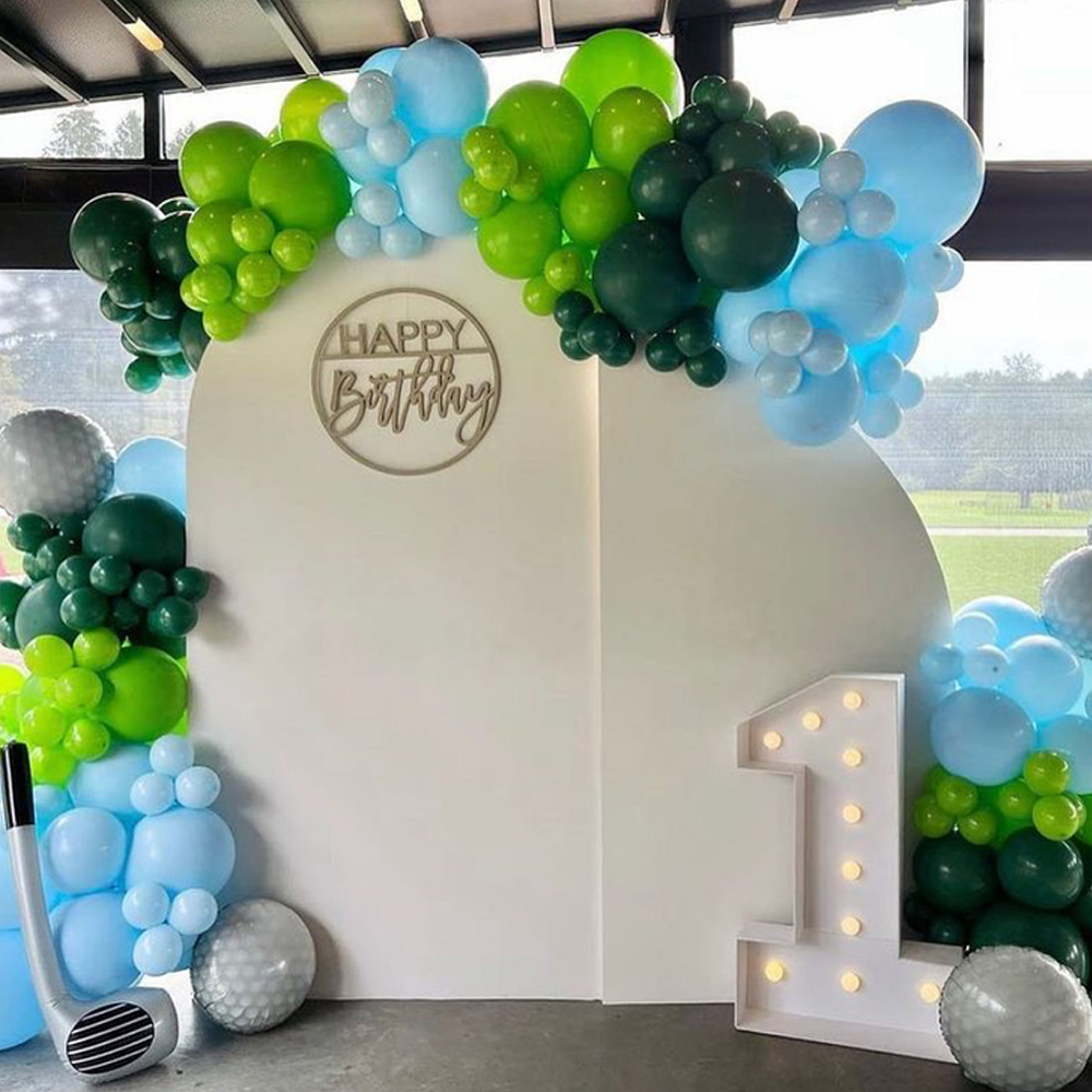 Birthday party decoration with green and blue balloon arch, a white backdrop with 'Happy Birthday' sign, and an illuminated number one.
