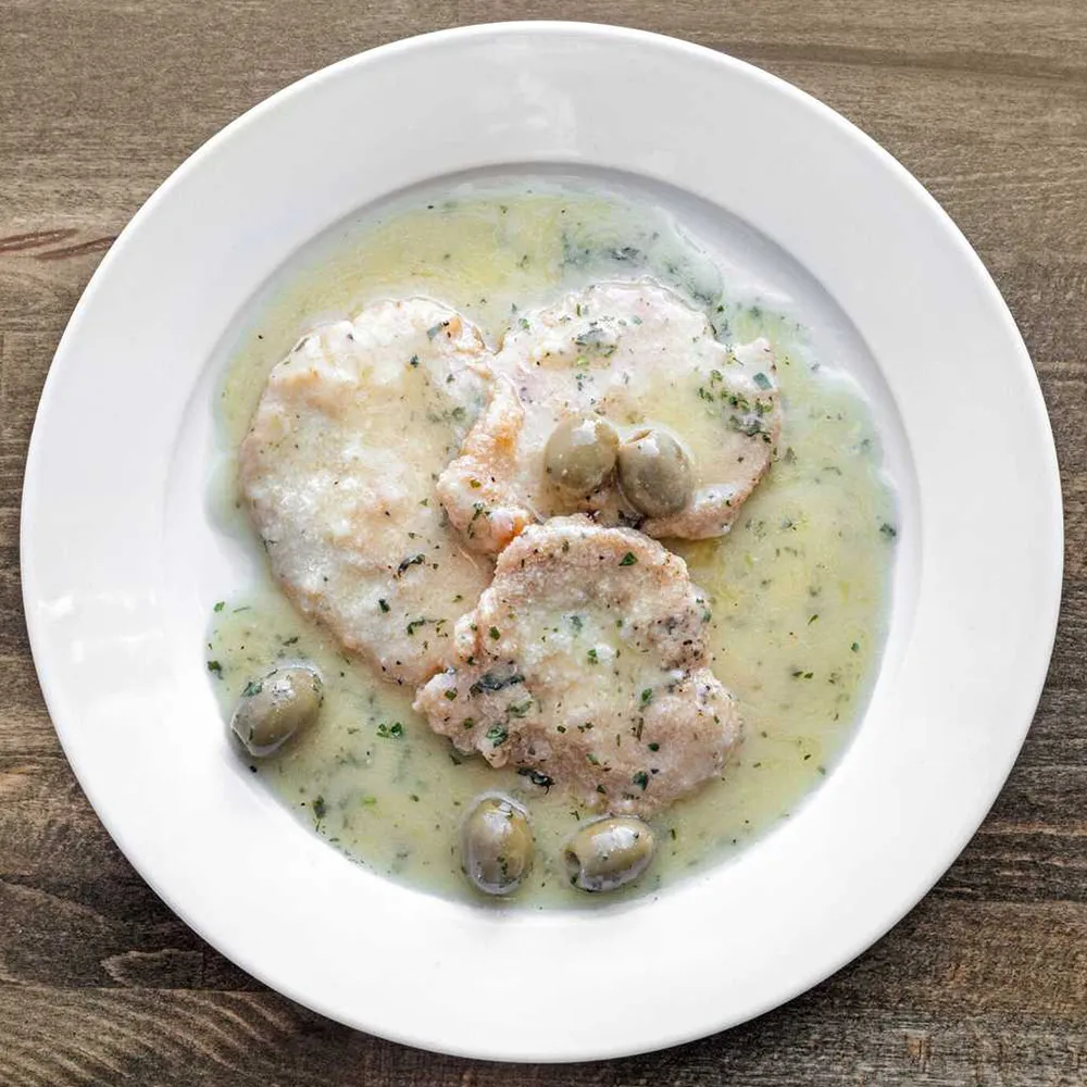 White plate with three pieces of chicken in creamy herb sauce garnished with green olives on a wooden surface.