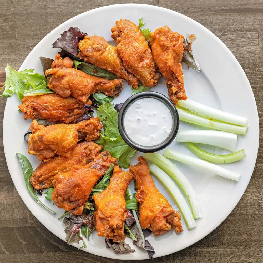 Plate of buffalo chicken wings with celery sticks, mixed greens, and a cup of ranch dressing.