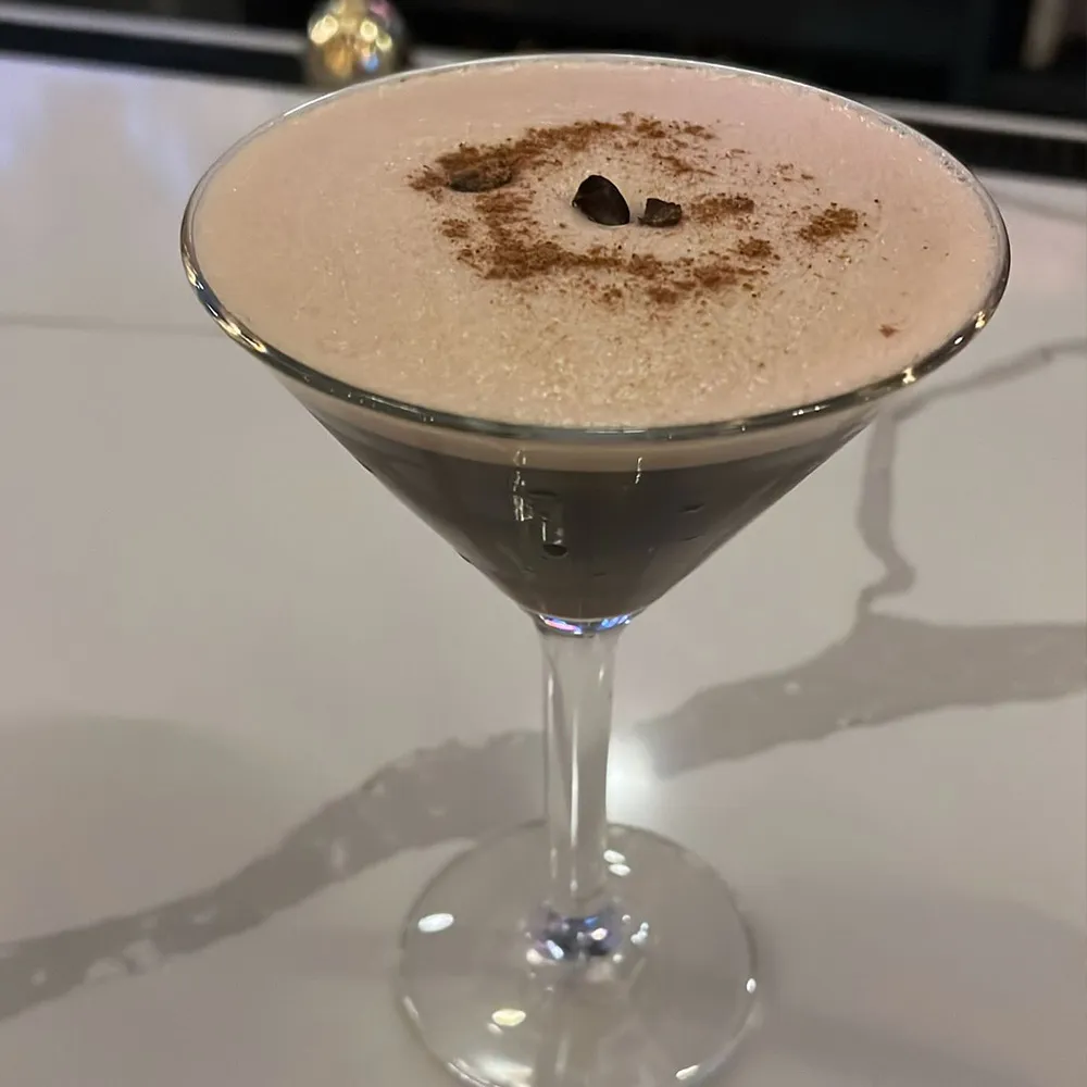 Martini glass filled with a frothy espresso cocktail garnished with coffee beans and a sprinkle of cocoa powder.