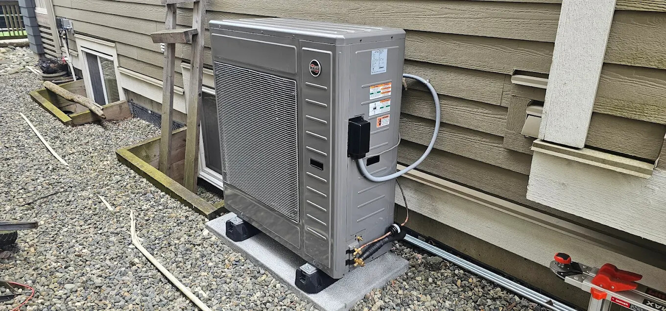 A modern exterior air-source heat pump unit installed on a concrete pad next to a residential home's siding.