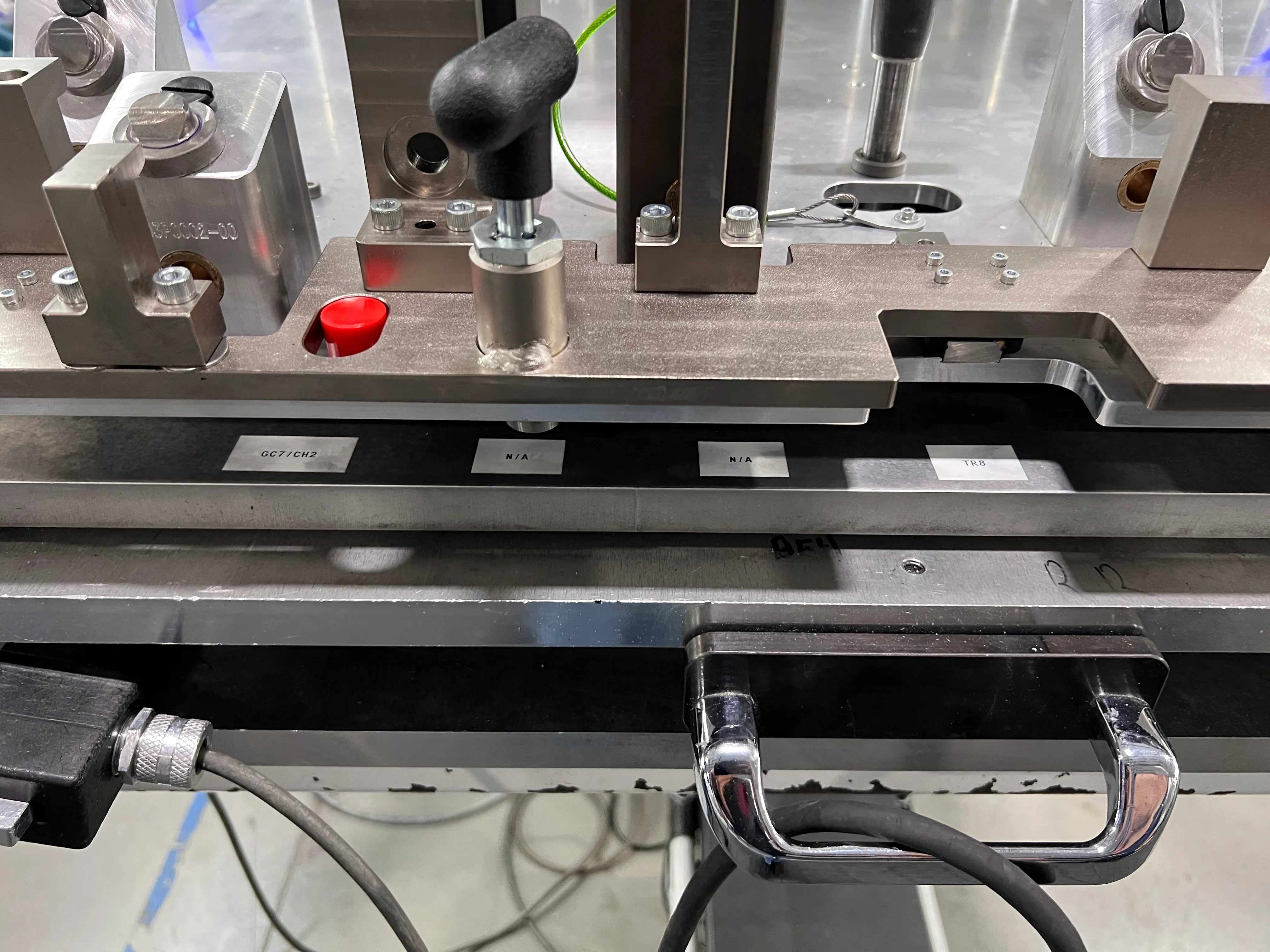 Close-up of a custom machine fixture with pneumatic clamps and labeled part positions