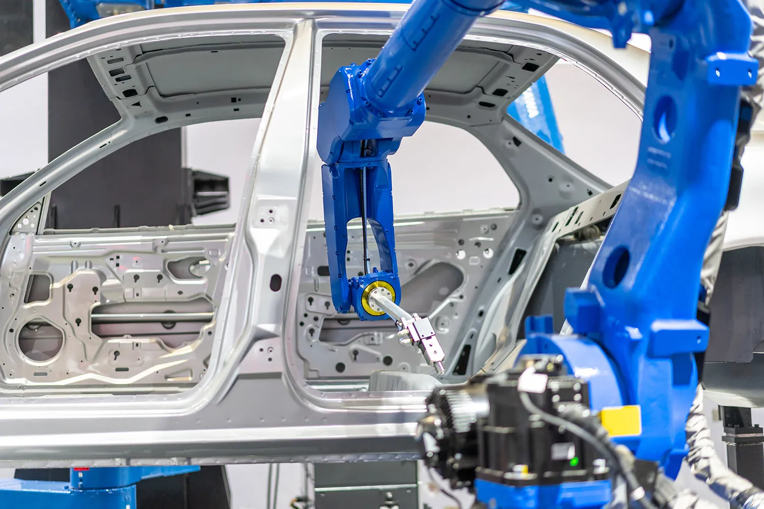 Blue robotic arm performing precision work on an automotive door frame