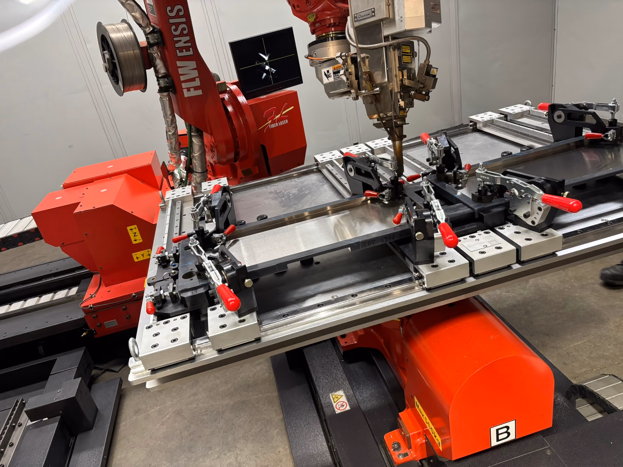 Robotic fiber laser welding arm positioned over a metal part in a custom tooling fixture