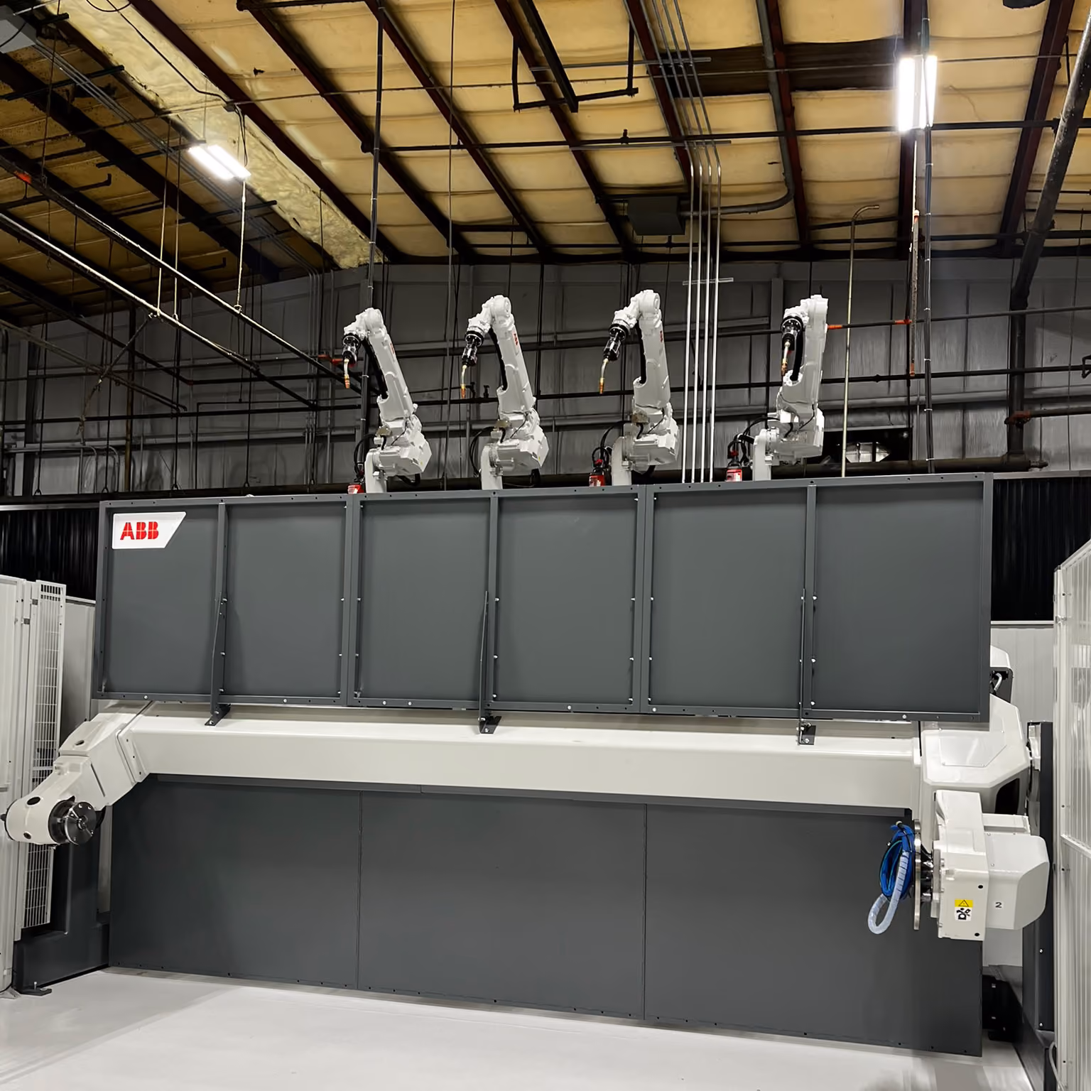 Four-arm ABB robotic welding cell mounted on an overhead gantry in a manufacturing facility