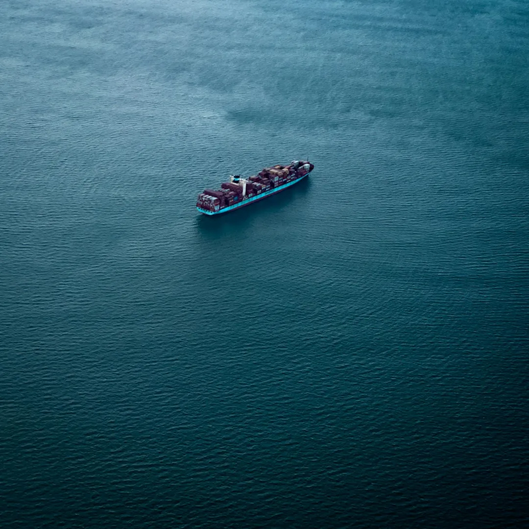 Cargo ship loaded with containers sailing on calm, deep blue water.