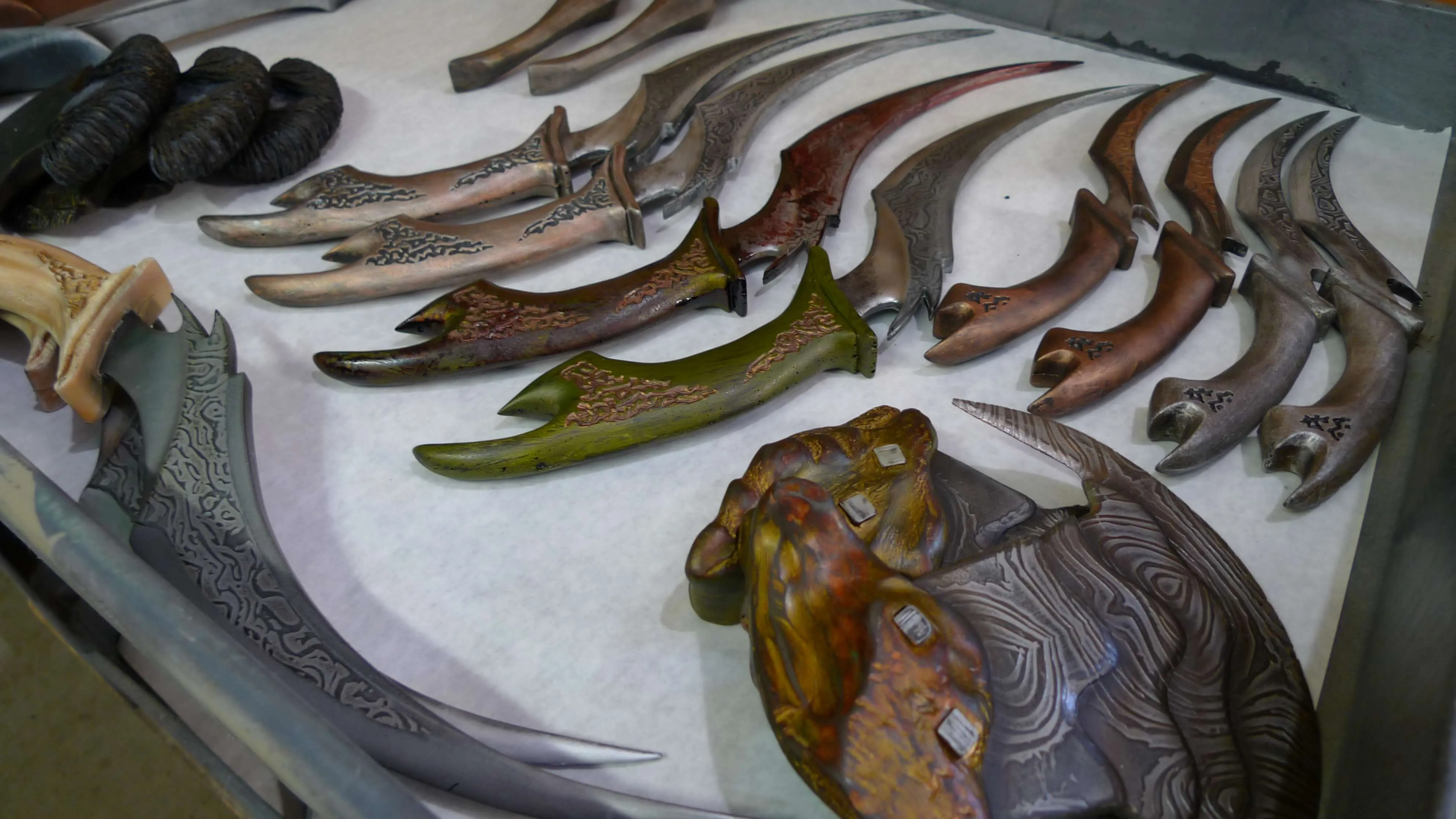 Collection of intricately designed curved knives with decorative handles and blades laid out on a white surface.