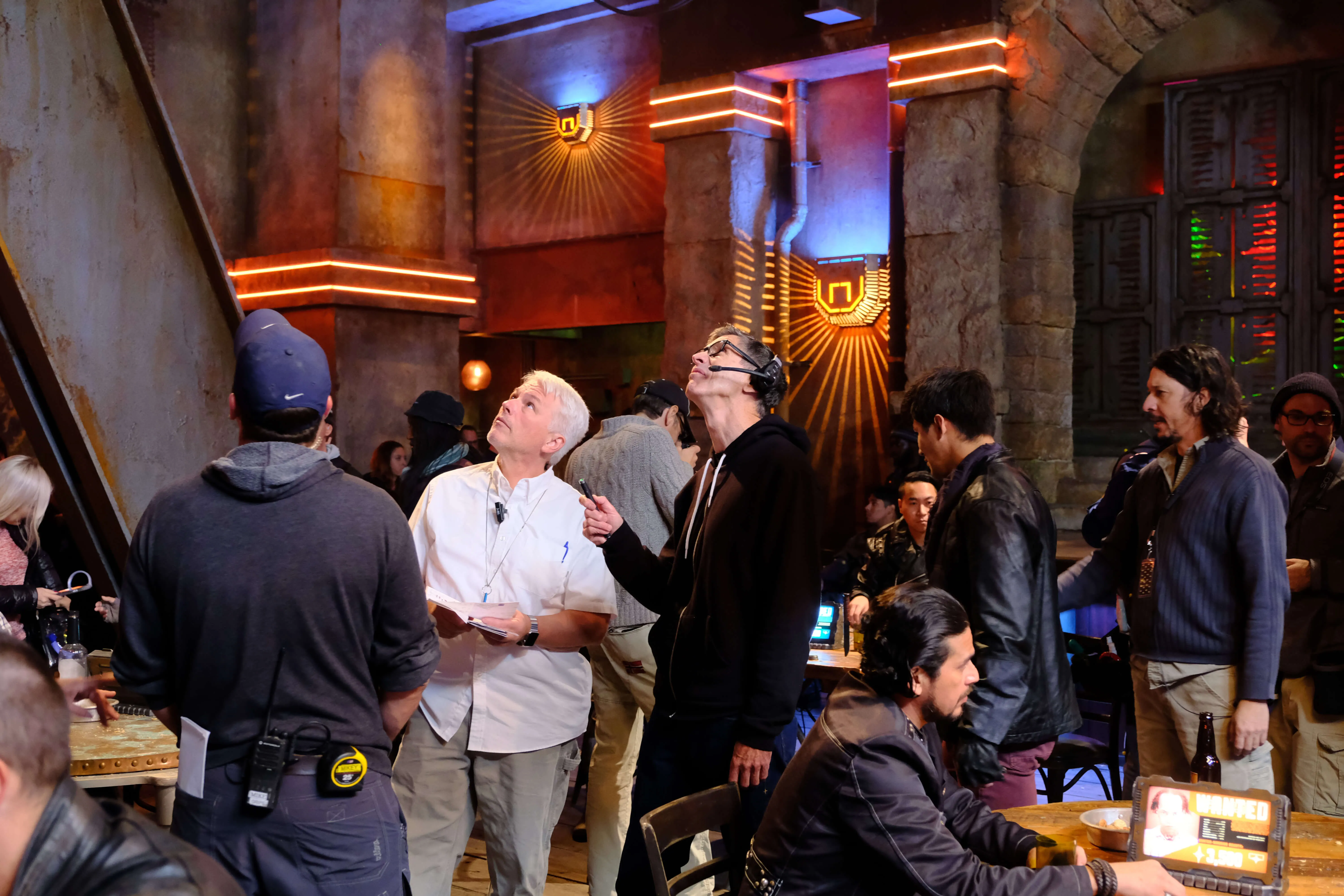 Group of people on a film set with crew members wearing headsets and holding scripts in a dimly lit room.