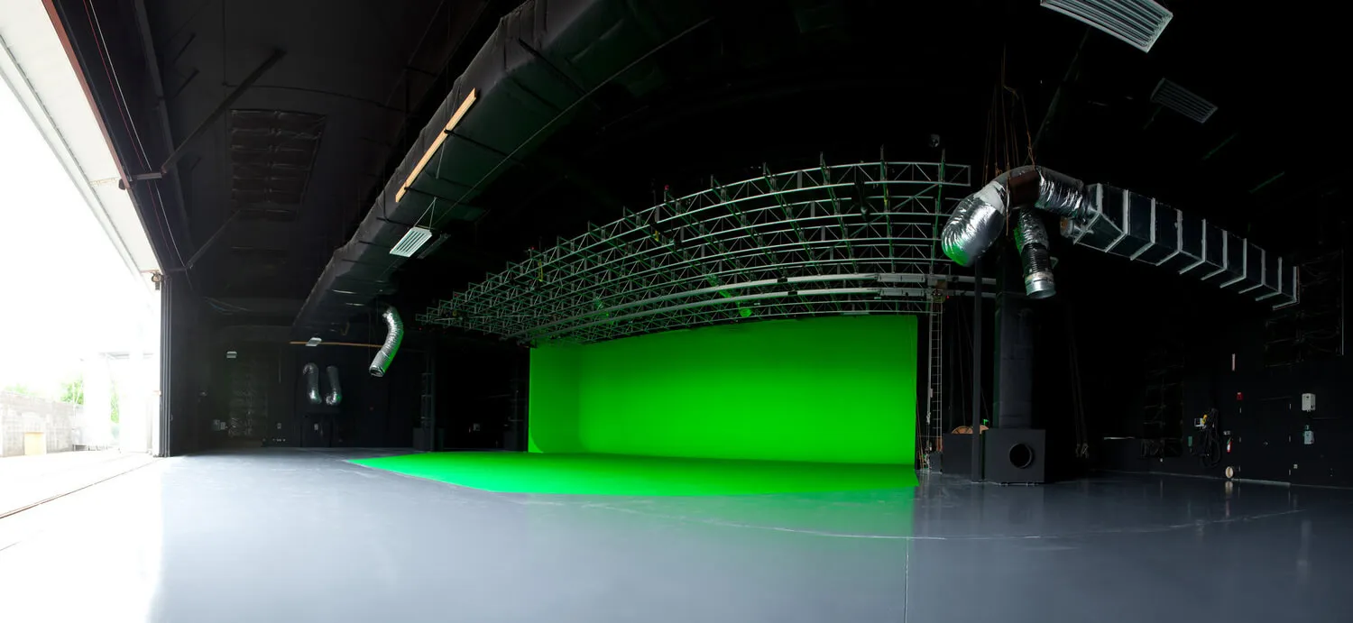 Empty film studio with a large green screen backdrop and glossy floor.