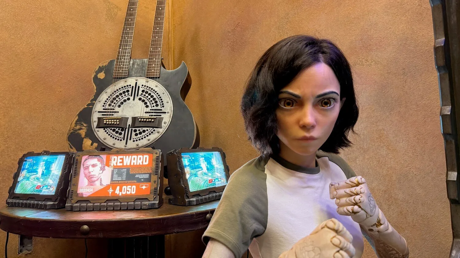 Robotic woman with short dark hair and detailed mechanical hands in a fighting pose, with two double-neck guitars and a reward sign on a wooden table behind her.