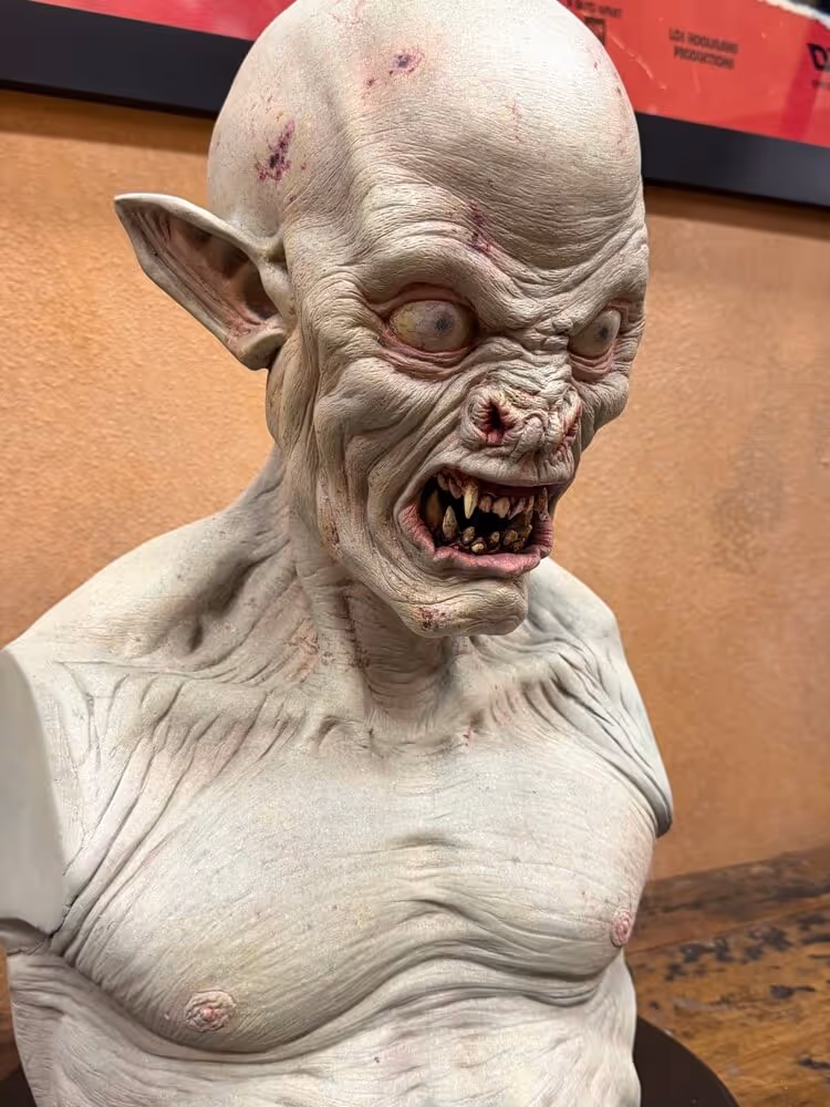 Bust sculpture of a pale, monstrous creature with pointed ears, sharp teeth, bulging eyes, and carved scars.
