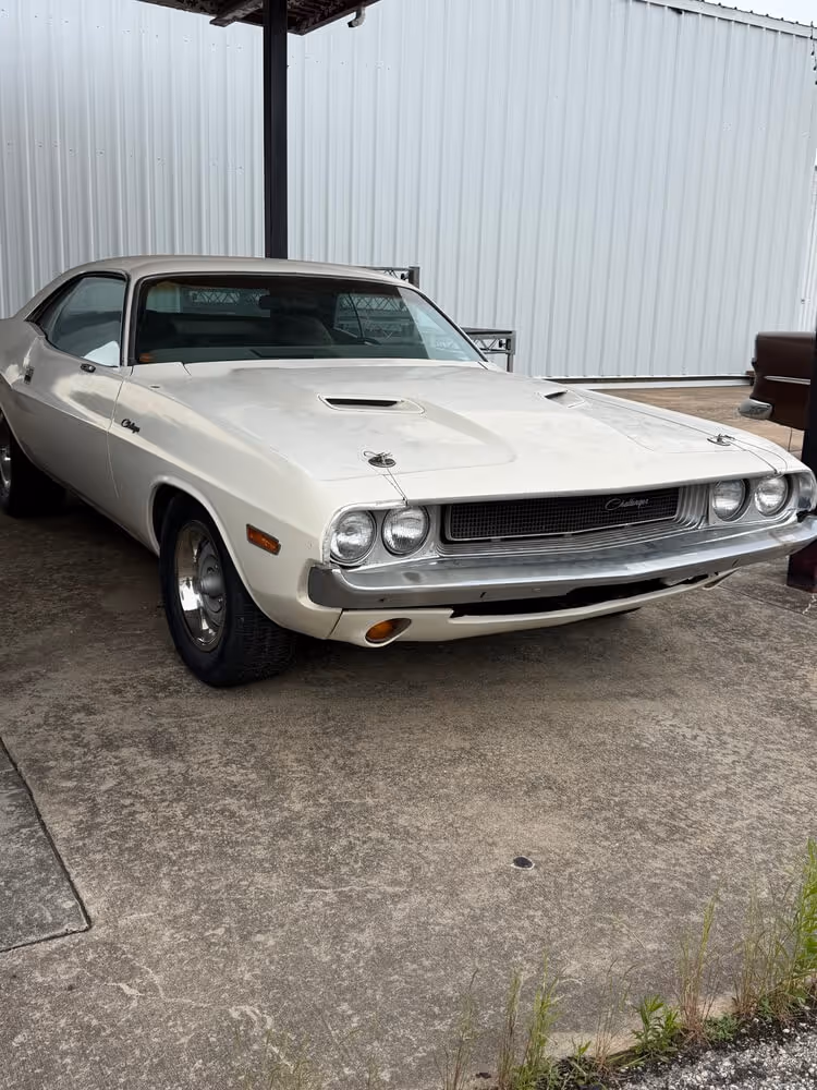 White classic Dodge Challenger parked on concrete under a metal carport.