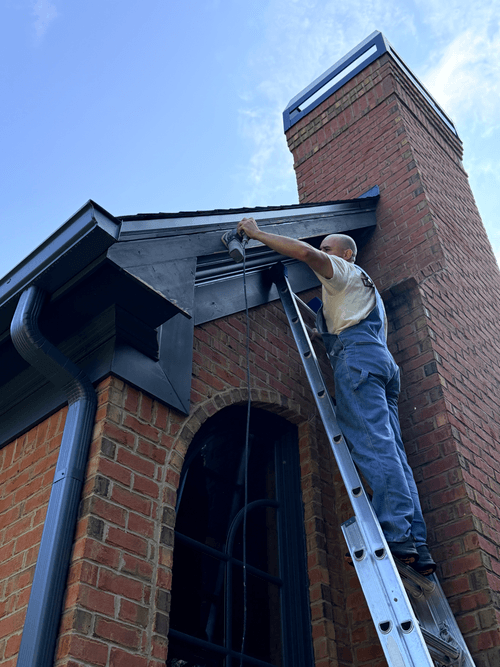 Sanding the worn paint off the chimney fascia boards from a ladder
