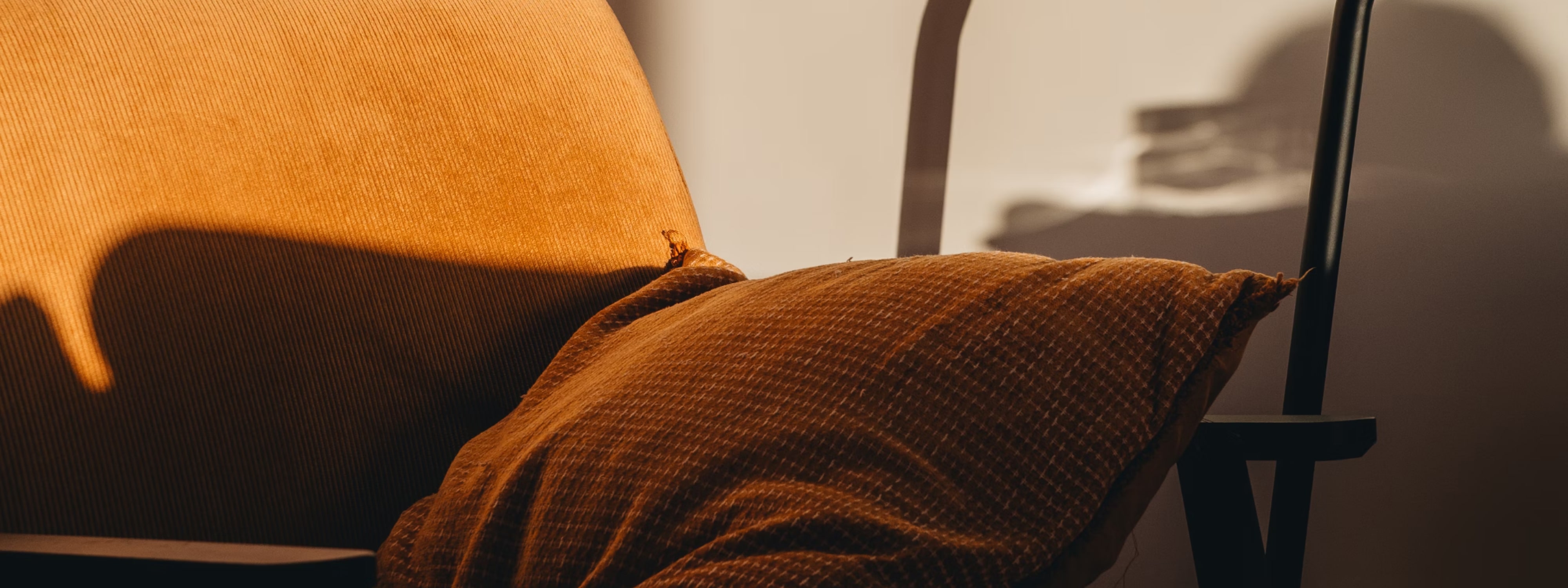 Orange-brown pillow resting against an orange-brown chair with shadows cast on both.