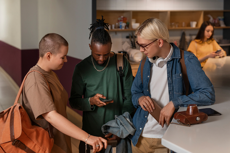 Three young adults indoors looking at phones and bags, with a woman using a smartphone behind them.