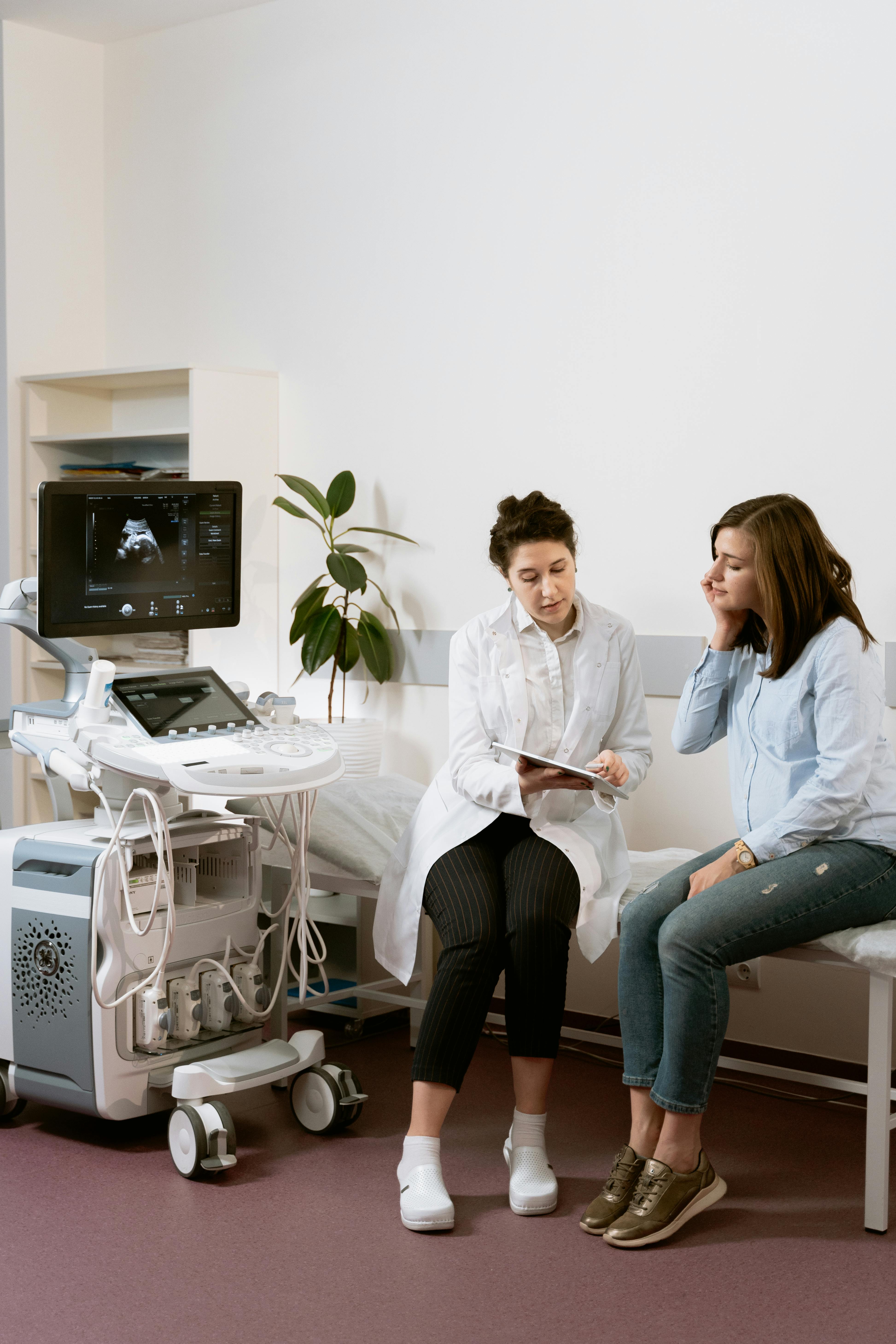 Doctor explains ultrasound results to a woman in a medical exam room with equipment visible.