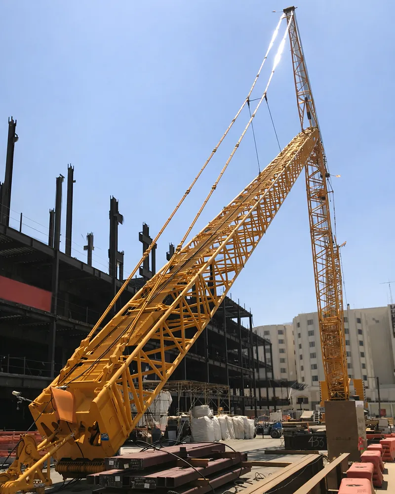 Construction crew in safety vests and hard hats gathered on an active jobsite under a tower crane for a daily briefing