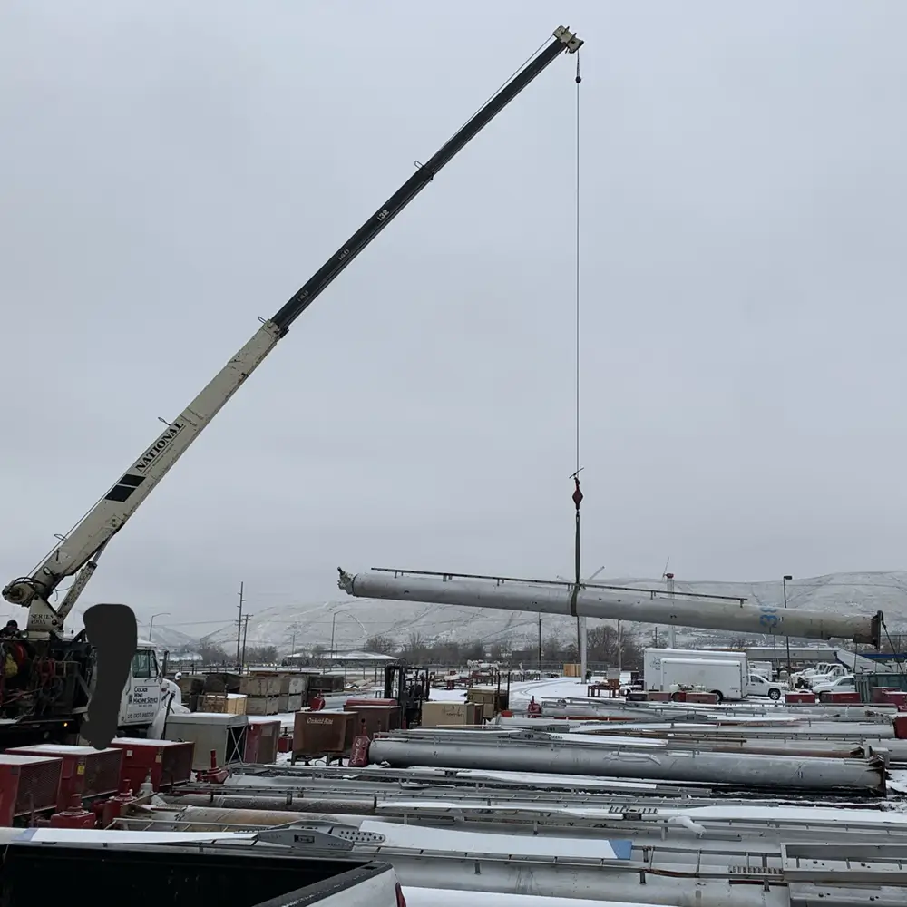 A National boom truck crane lifting a wind machine tower section at Cascade Wind Machine in a snowy Central Washington yard.