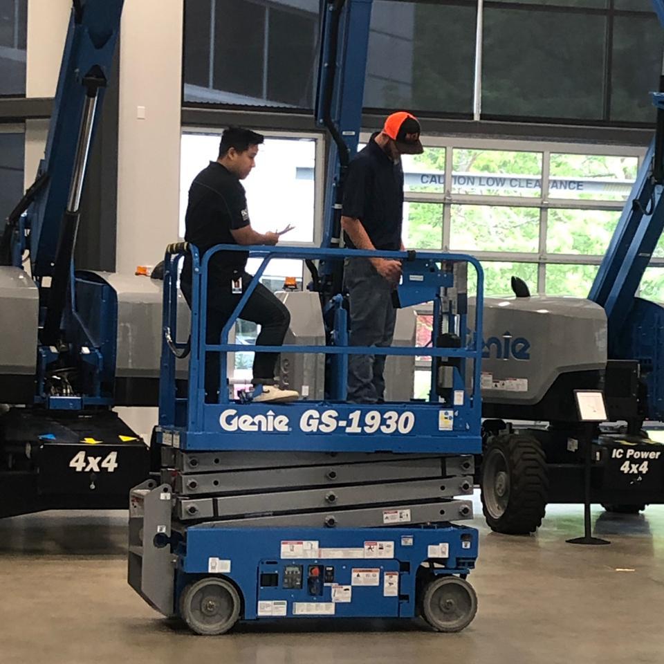 Andrew Lange of A/F Business Solutions at the controls of a Genie GS-1930 scissor lift while a trainee on the platform reviews an evaluation form.