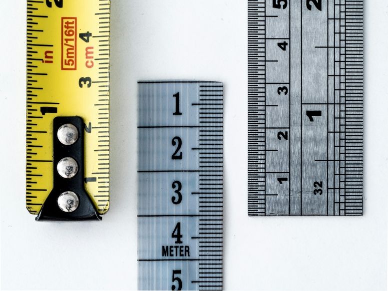 Drei verschiedene Lineale nebeneinander: ein gelbes Maßband in Zoll und Zentimetern, ein durchsichtiges Maßband in Metern und ein Metalllineal in Zentimetern und Millimetern.